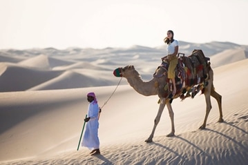 Frau reitet auf einem Kamel durch die Wüste
