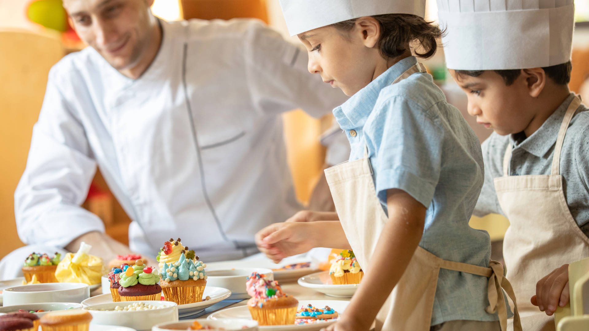 Image of two small children, dressed in aprons and chef hats, decorating cupcakes at Madinat Jumeirah