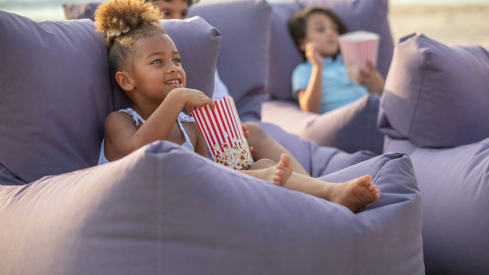 Image of a small girl enjoying popcorn, sat on a large purple beanbag at Madinat Jumeirah's outside cinema