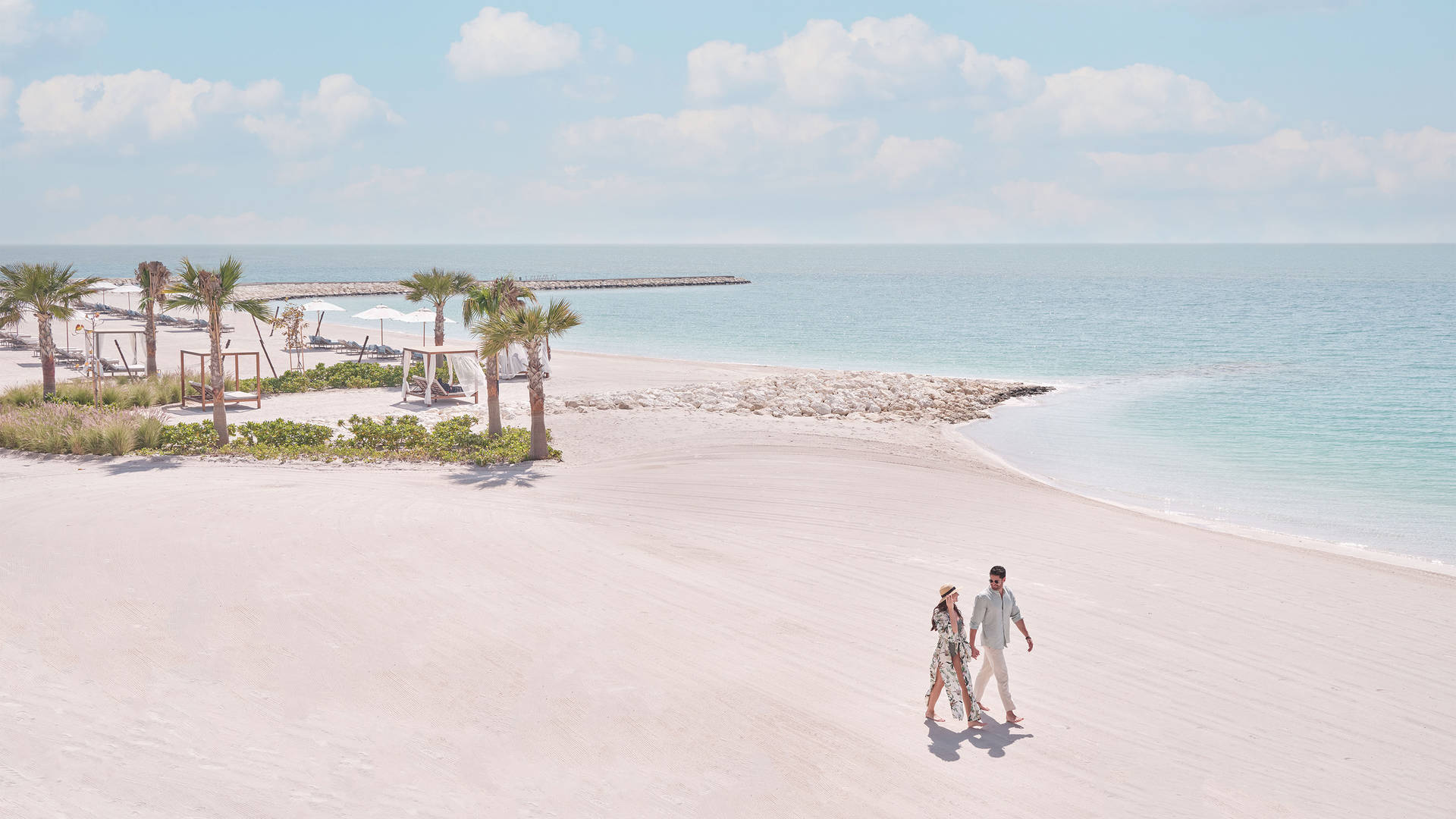 Couple walking along the beach at Jumeirah Gulf of Bahrain Resort and Spa