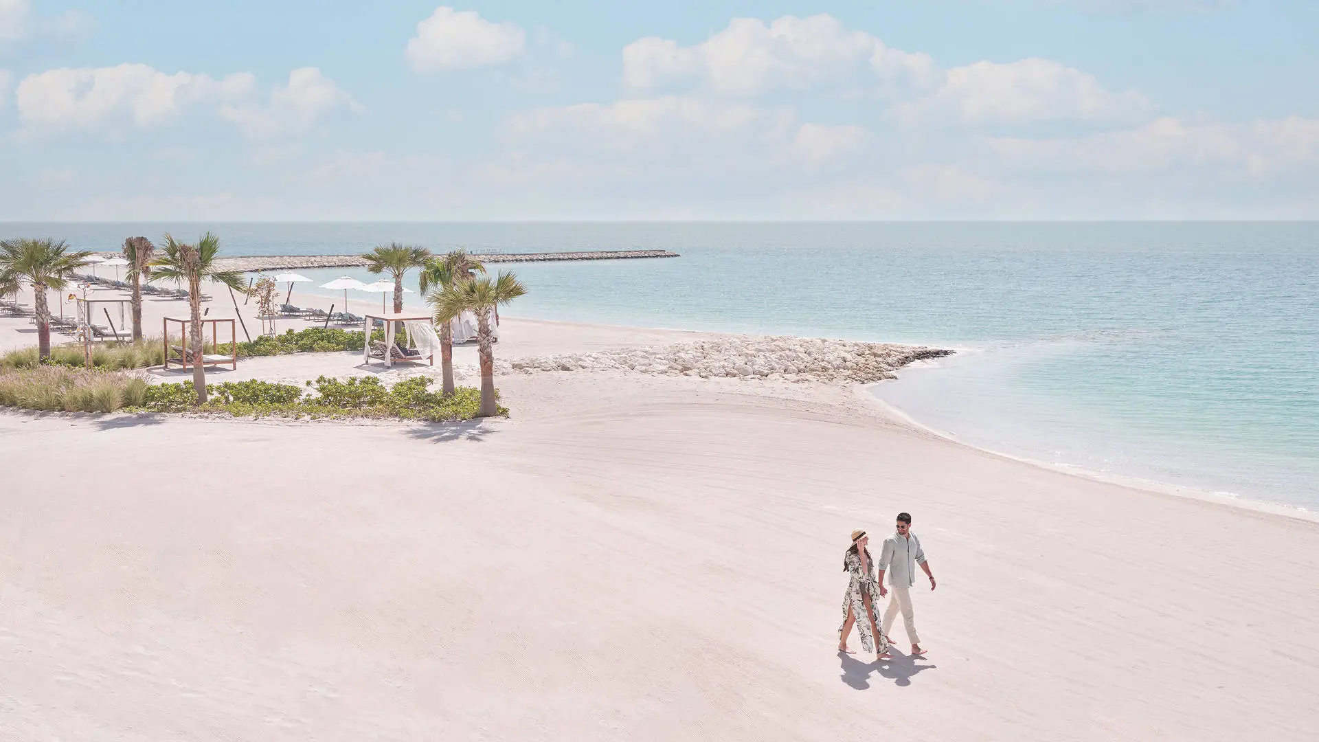 Couple walking along the beach at Jumeirah Gulf of Bahrain Resort and Spa